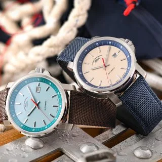 Zwei Armbanduhren (29er Big mit südseeblauem Zifferblatt und 29er Big mit sandfarbenem Zifferblatt) liegen auf Metallstücken und Seilen.