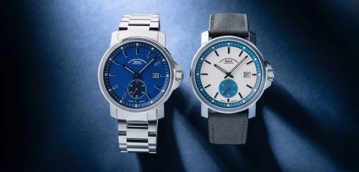 The 29er Big Small Seconds with blue dial and metal bracelet and the 29er Big Small Seconds with white-petroleum dial and grey strap lie side by side on a blue background