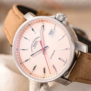 Nahaufnahme der Armbanduhr "29er" mit apricotfarbenem Zifferblatt am sandfarbenen Canvasband seitlich liegend.