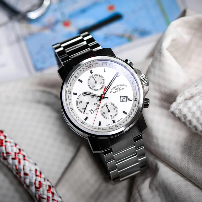 29er Chronograph mit weißem Zifferblatt und Metallband liegt auf hellem Stoff.