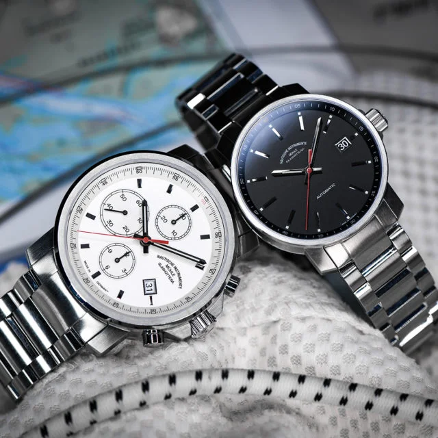 Zwei Armbanduhren (29er Chronograph mit weißem Zifferblatt, 29er mit schwarzem Zifferblatt) liegen auf weißem Stoff.