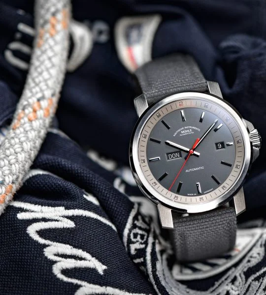 Herrenarmbanduhr 29er Big Tag/Datum mit grauem Zifferblatt am grauen Canvasband steht leicht seitlich auf blau-weißen Stoffen und Seilen.