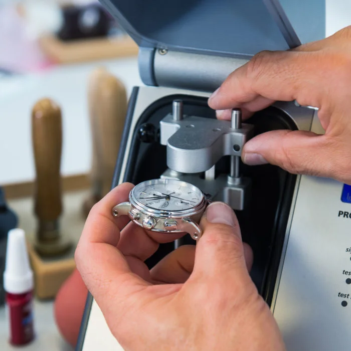 Zwei Hände legen eine Uhr in die Prüfmaschine für die Wasserdichte.