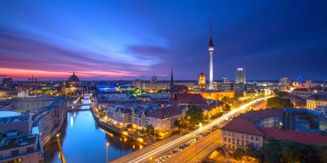 Berliner Skyline bei Nacht mit Straßenlichtern. Im Hintergrund der Fernsehturm vor dunkelblauem Himmel.