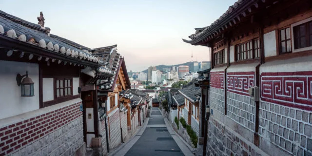 Stadtaufnahme von Seoul. In der Mitte eine Straße, am Rand traditionelle Gebäude. Im Hintergrund die moderne Skyline.