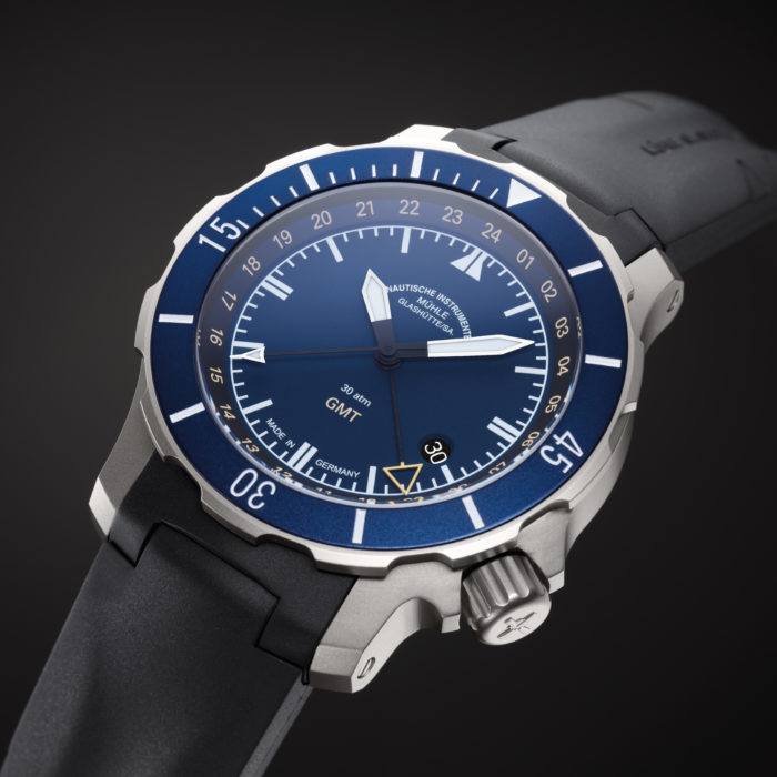 Seebataillion GMT, eine Armbanduhr mit blauem Zifferblatt und Lünette im mattsilbernen Gehäuse am schwarzen Band, liegt vor schwarzem Grund