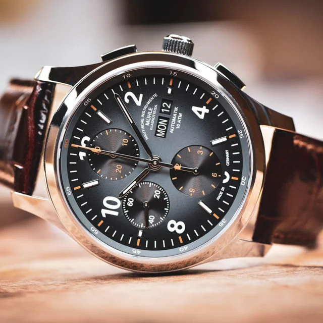 Armbanduhr Lunova Chronograph am braunen Krokolederband liegt seitlich auf einem Holztisch.