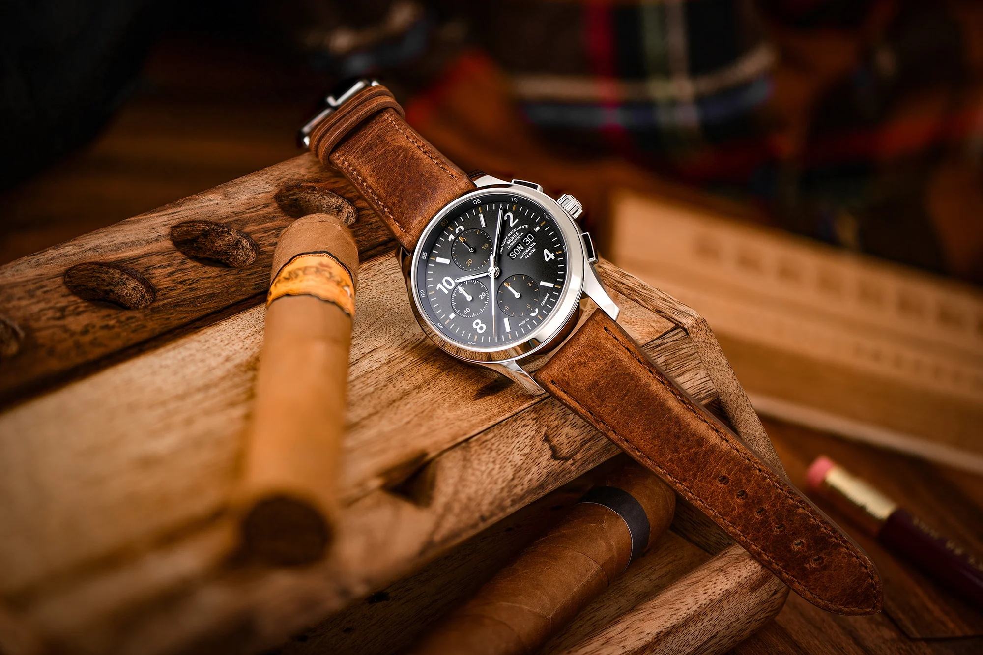 Armbanduhr Lunova Chronograph am braunen Vintagelederband liegt auf einem Holzetui neben einer Zigarre.
