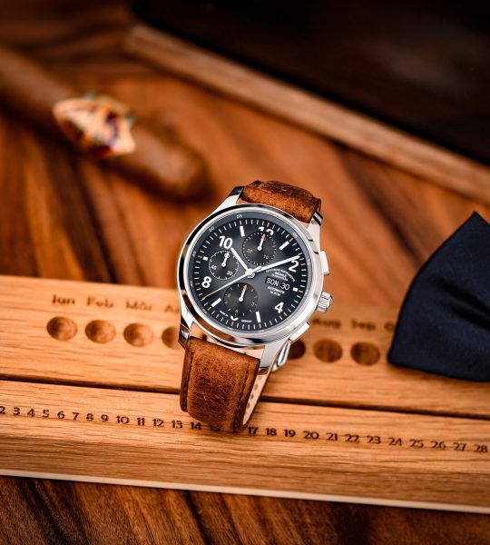 Armbanduhr Lunova Chronograph am braunen Vintagelederband steht auf einem Holzlineal auf einem Holztisch