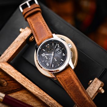 Armbanduhr Lunova Chronograph am braunen Vintagelederband liegt auf verschiedenen Holzteilen und einem schwarzen Lederetui.