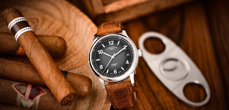 Armbanduhr Lunova Datum am braunen Vintagelederband steht auf einem Holztisch, daneben eine Schalte mit Zigarren.