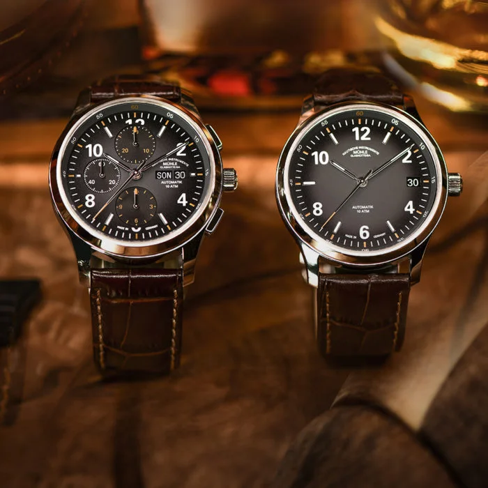 Lunova Chronograph und Lunova Datum an braunen Krokolederbändern stehen auf einem Holztisch mit verschwimmenden Konturen.