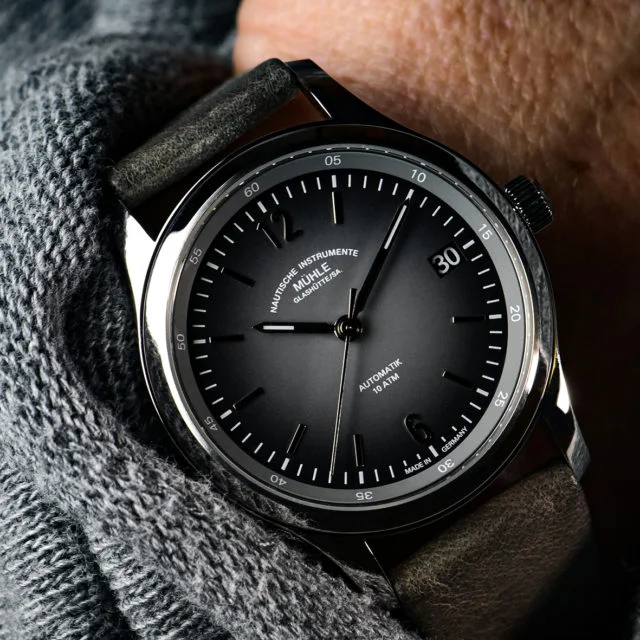 Armbanduhr Lunova Lady am grauen Lederband am Handgelenk mit grauem Pullover.