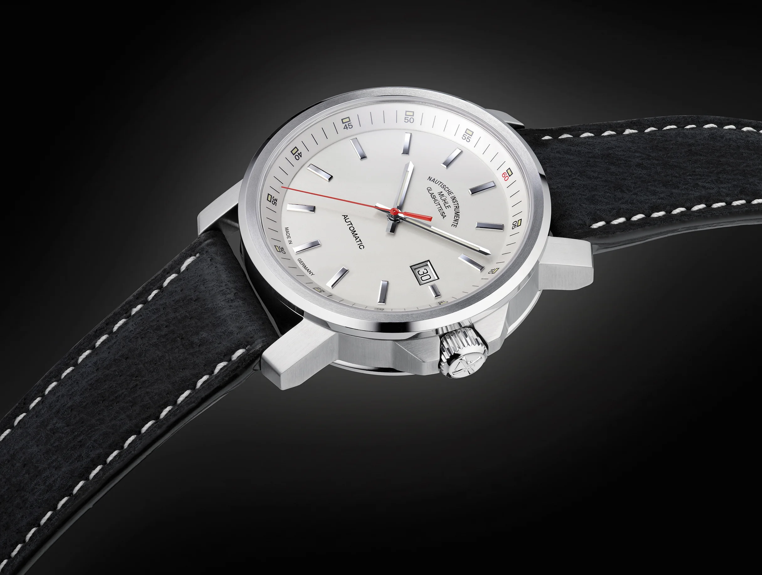 Armbanduhr "29er Big" mit weißem Zifferblatt am schwarzen Lederband vor schwarzem Hintergrund.