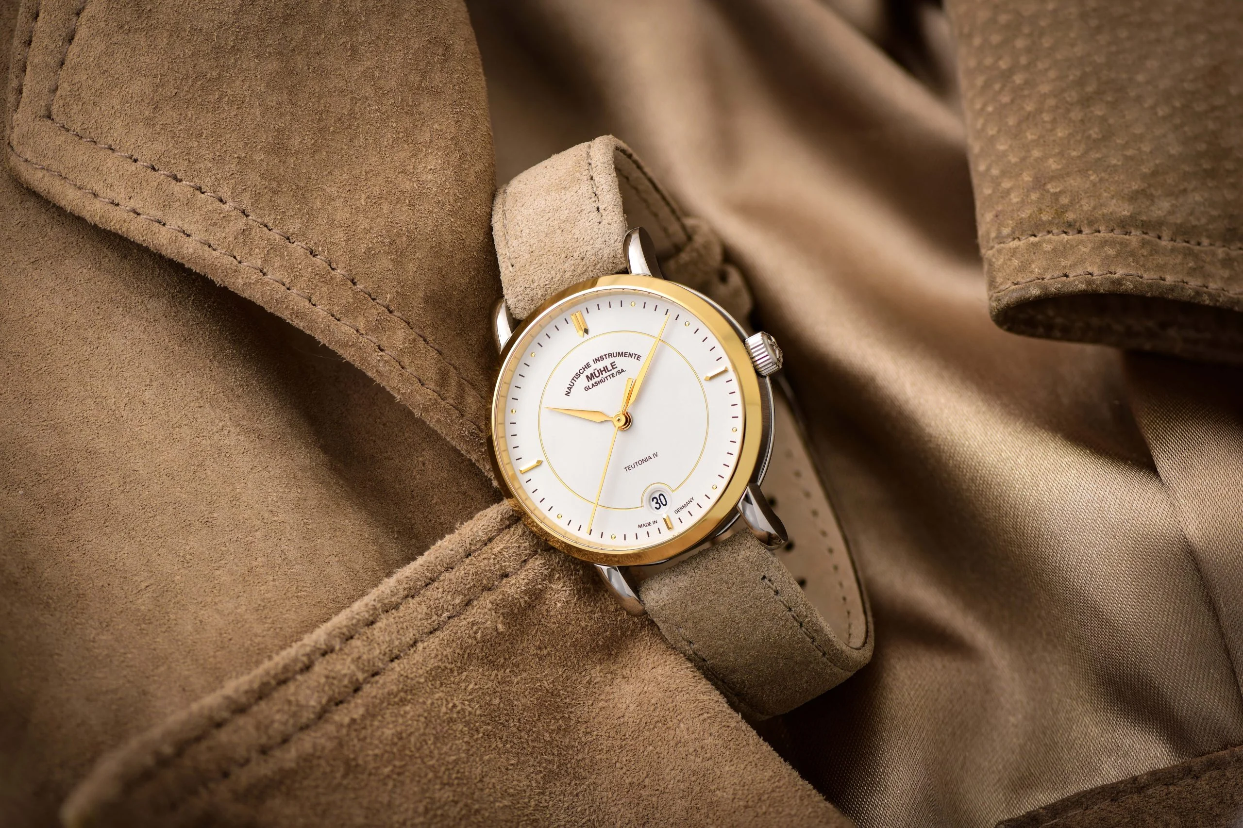 Armbanduhr Teutonia IV Lady mit weißem Zifferblatt am beigen Veloursband liegt leicht schräg auf einem hellbraunen Wildlederjacke.