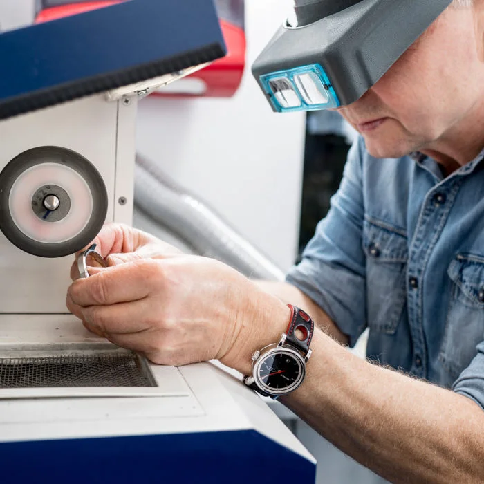 Ein Mitarbeiter mit Spezialbrille bearbeitet ein Gehäuse an einer Schleifmaschine.