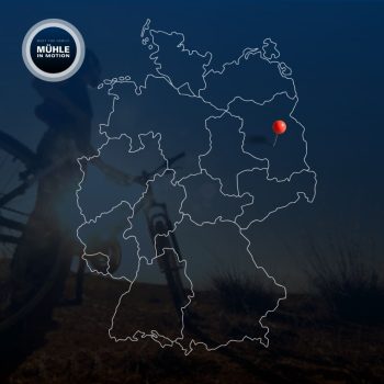 Weiße Umrisse einer Deutschlandkarte auf blauem Hintergrund. Dahinter ein Radfahrer vor einem Sonnenuntergang.