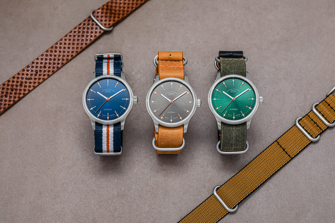 Drei Armbanduhren (Panova blau, grau und grün) liegen mit zwei zusätzlichen Bändern auf einem grauen Tisch.