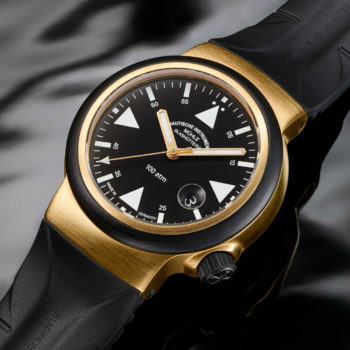 S.A.R. Rescue-Timer GOLD: Eine Armbanduhr mit schwarzem Zifferblatt, weißen Indizes und goldenem Gehäuse liegt auf einem schwarten, welligen Untergrund.