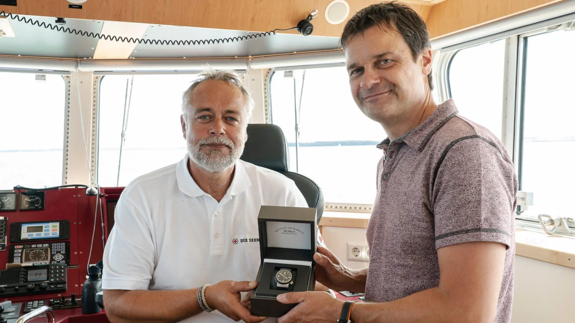 Thilo Mühle (rechts) übergibt einen S.A.R. Rescue-Timer in einer schwarzen Box an einen Vormann der DGzRS.