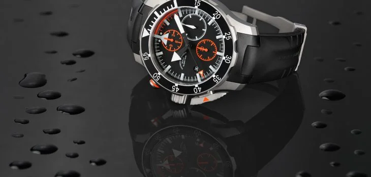 The S.A.R. pilot's chronograph with black rubber strap lies on its side on a black, reflective surface.