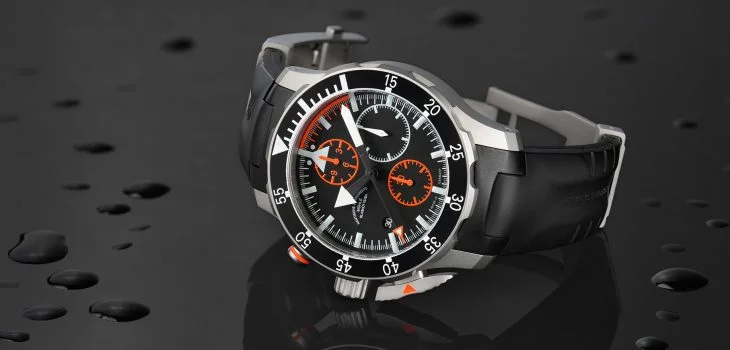 S.A.R. Flieger-Chronograph mit schwarzem Kautschukband liegt seitlich auf einer schwarzen, spiegelnden Oberfläche.