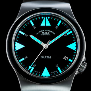 Zifferblatt des S.A.R. Mission-Timers: Armbanduhr mit schwarzem Zifferblatt, blau-grün nachleuchtenden Indizes und Zeiger, schwarze Kautschuklünette und mattsilbernes Gehäuse.