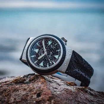 Nasser S.A.R. Rescue-Timer am schwarzem Kautschukband liegt auf einem Felsen vorm Meer.