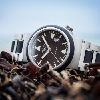 S.A.R. Rescue-Timer mit schwarzem Zifferblatt am Metall-/Kautschukband liegt seitlich auf einem Haufen brauner Algen.