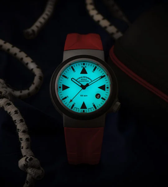 Nachtansicht des S.A.R. Rescue-Timer LUMEN mit rotem Kautschukband und blau-grün nachleuchtendem Zifferblatt
