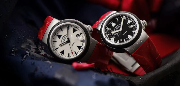Zwei Armbanduhren (S.A.R. Rescue-Timer LUMEN und S.A.R. Rescue-Timer) mit rotem Kautschukband liegen seitlich auf blau-roter Segelbekleidung.