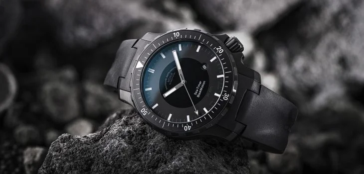 Armbanduhr Sea-Timer BlackMotion am schwarzen Kautschukband liegt seitlich auf einem schwarzen Stein.