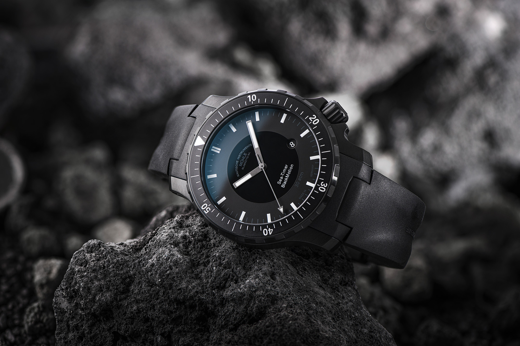 Armbanduhr "Sea-Timer BlackMotion" liegt seitlich auf einem dunklen Stein.