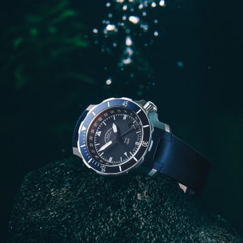 Seebataillon GMT am blauen Kautschukband liegt seitlich auf einem Stein im Wasser.