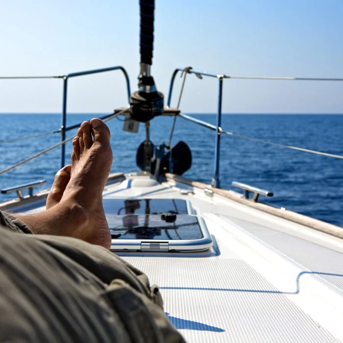 Bug einer Segelyacht bei ruhiger See mit angeschnittenem Mann, der die Füße übereinander gelegt hat