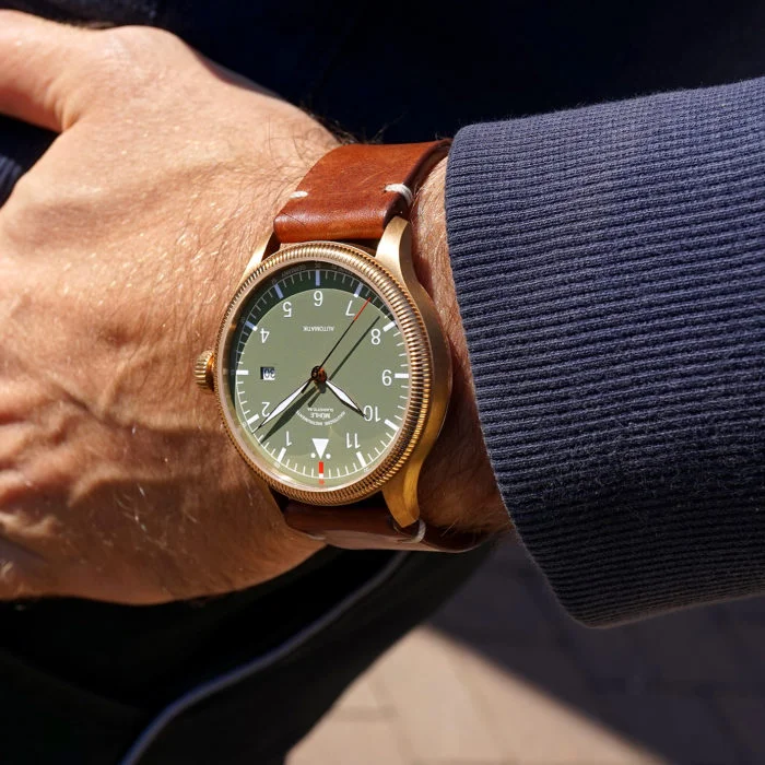 Wristshot Terrasport Bronze: Armbanduhr mit grünem Zifferblatt, bronzefarbenem Gehäuse und braunem Lederband an einem Handgelenk.