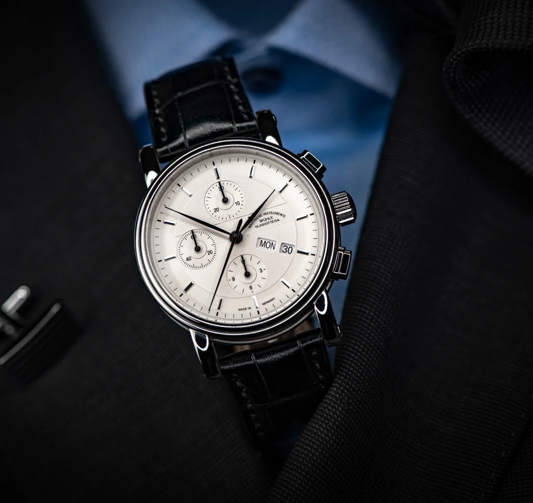 Armbanduhr Teutonia II Chronograph am schwarzen Lederband steht auf einem schwarzen Sakko mit hellblauem Hemd.
