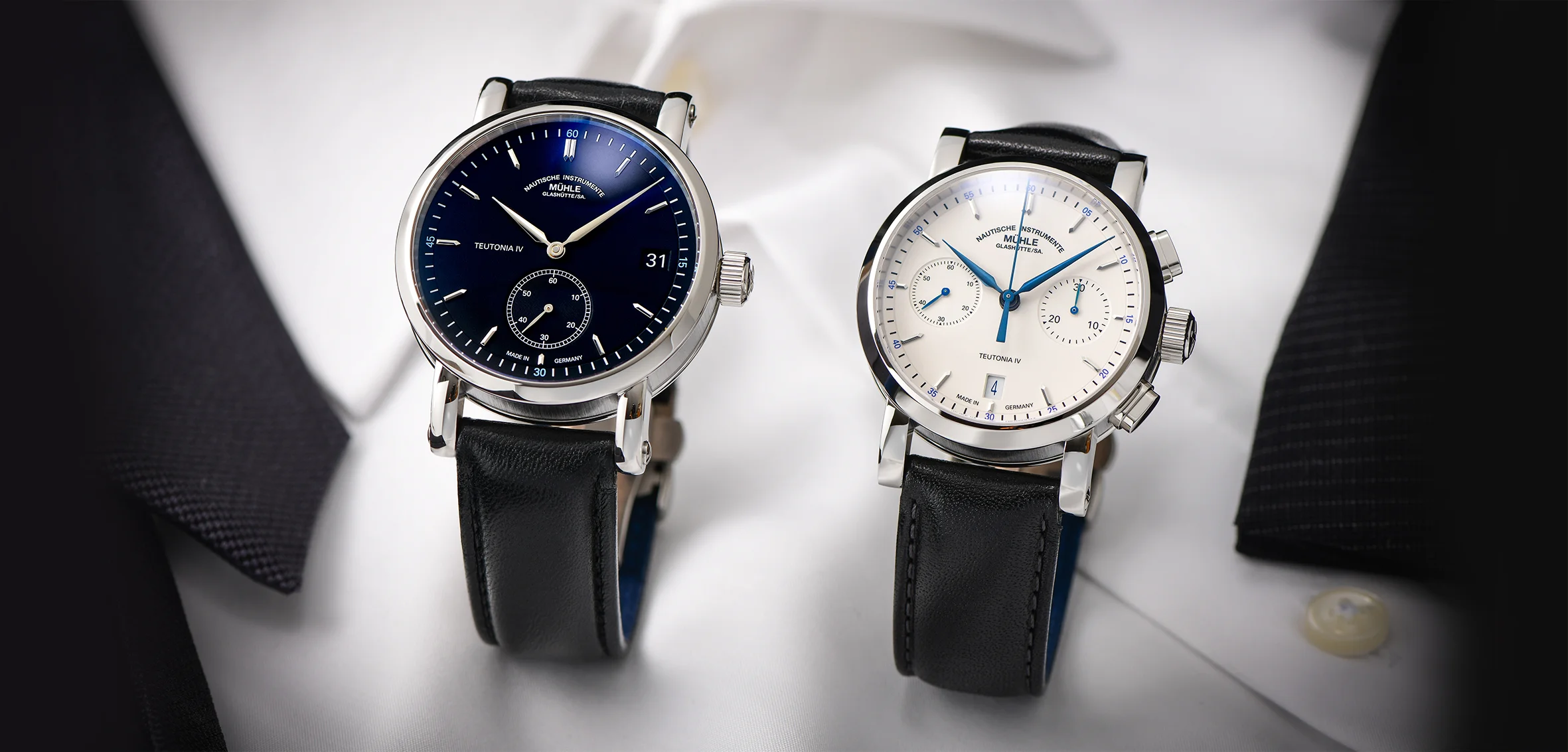 Zwei Armbanduhren (Teutonia IV Kleine Sekunde und Teutonia IV Chronograph, beide am schwarzen Lederband) stehen auf einem weißen Herrenhemd mit schwarzem Sakko.