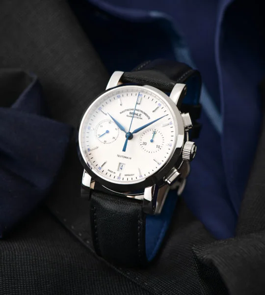 Armbanduhr Teutonia IV Chronograph am schwarzen Lederband steht auf einem schwarzen Anzug mit dunkelblauem Hemd.