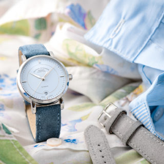 Armbanduhr Teutonia IV Lady mit pastellblauem Zifferblatt am blauen Veloursband steht auf weiß-grünem und hellblauen Stoffen.