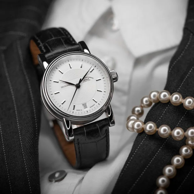 Armbanduhr Teutonia II Medium mit weißem Zifferblatt am schwarzen Lederband steht auf einem weißen Herrenhemd und schwarzem Sakko.