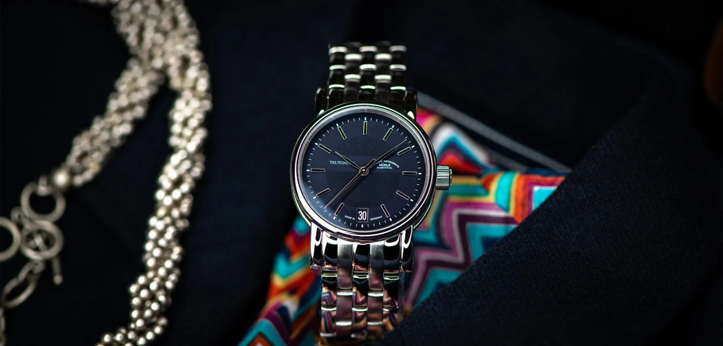 Armbanduhr Teutonia II Medium mit blauem Zifferblatt am Metallband steht auf einem bunt gemusterten Schlips und einem dunklen Sakko.