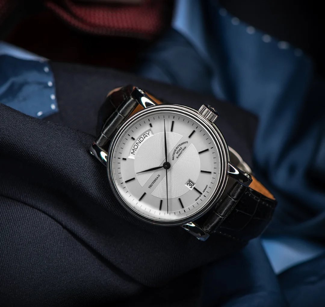 Armbanduhr Teutonia II Tag/Datum lieht leicht schräg auf grauem und blauem Stoff.