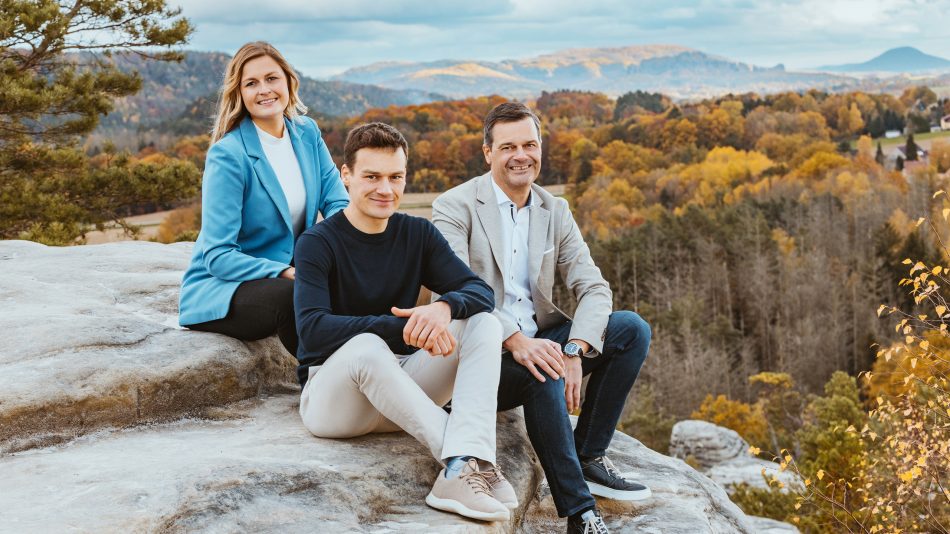 V.l.n.r.: Fanny, Dustin und Thilo Mühle sitzen auf einem Felsen im Elbsandsteingebirge mit Wald im Hintergrund.