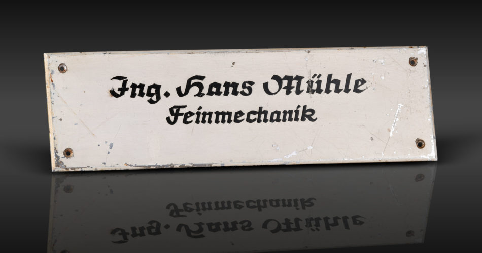 Weißes Namensschild mit schwarzer Schrift steht auf einer glänzenden schwarzen Oberfläche.