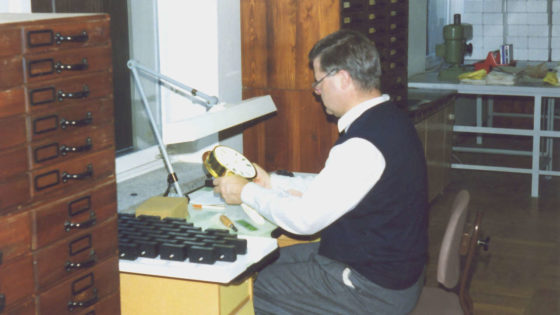 Hans-Jürgen Mühle sitzt an einem Tisch und stellt eine Schiffsuhr ein.