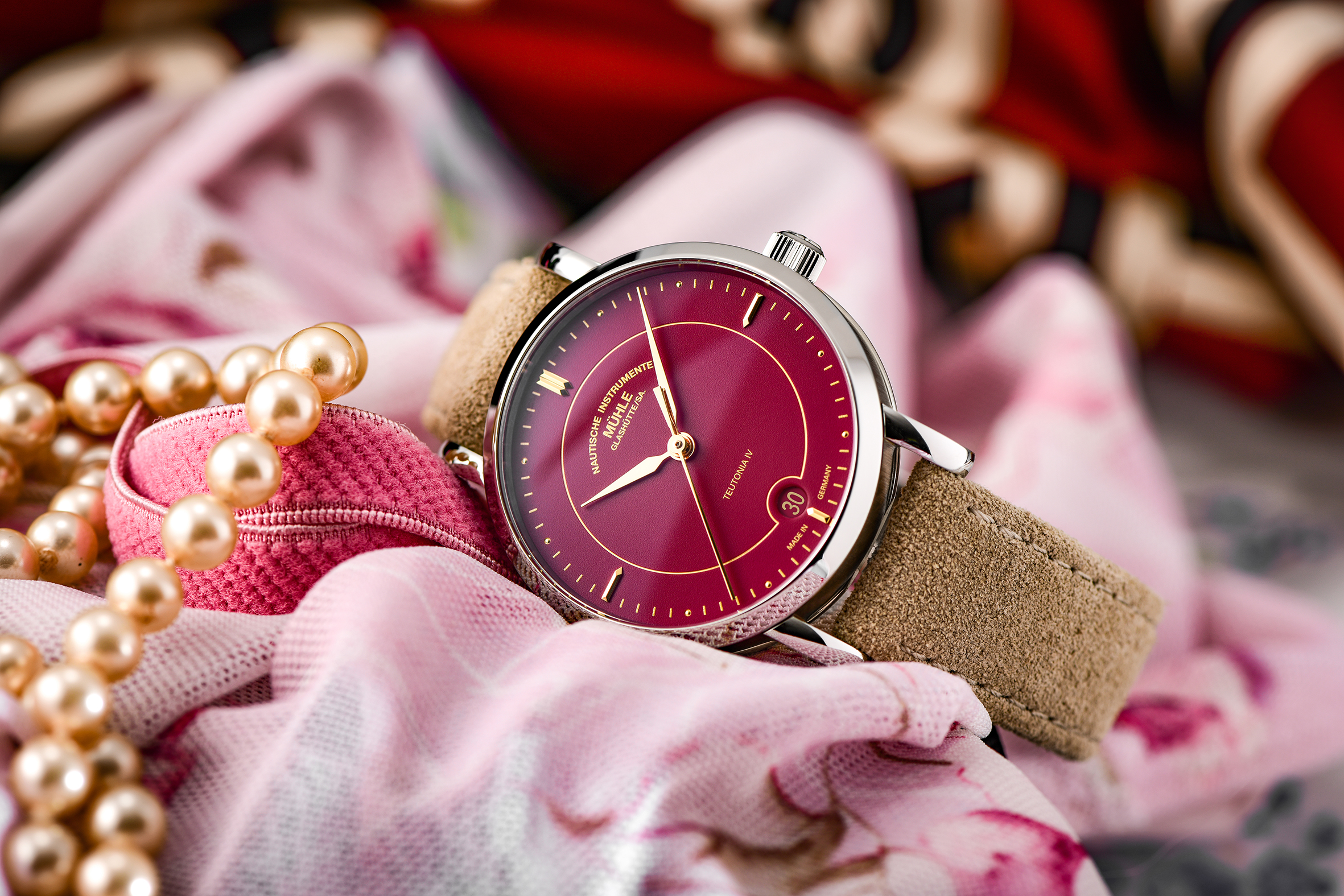 Armbanduhr Teutonia IV Lady mit himbeerrotem Zifferblatt am beigen Veloursband liegt seitlich auf einem rosafarbenem Tuch.