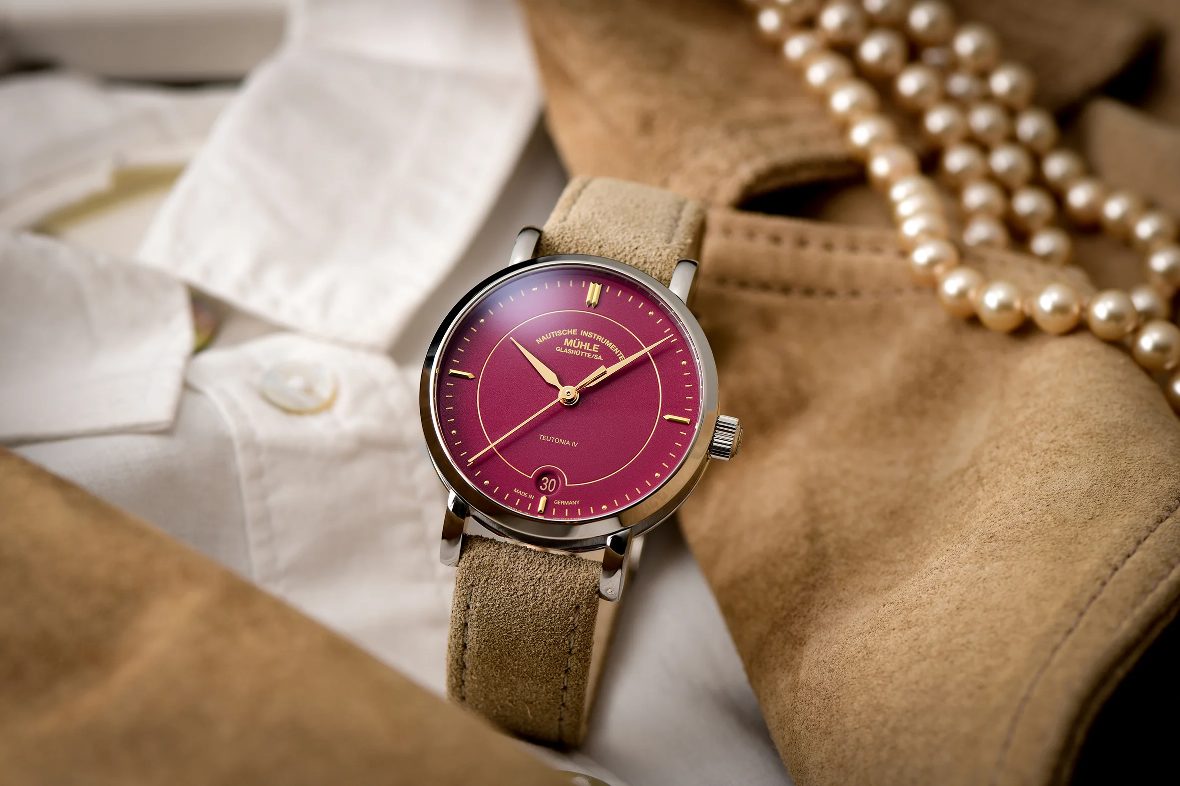 Armbanduhr Teutonia IV Lady mit himbeerrotem Zifferblatt am beigen Veloursband steht auf einer weißen Damenbluse und einer hellbraunen Wildlederjacke.