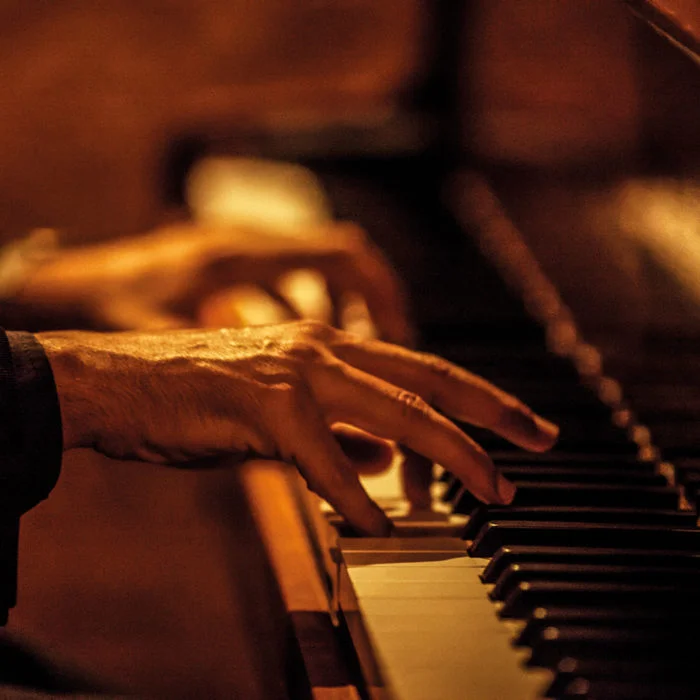 Zwei Hände, die Klavier spielen in warm-orangem Licht.