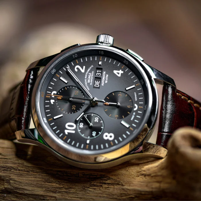 A Lunova Chronograph wristwatch on a brown leather strap lies sideways on a piece of wood.